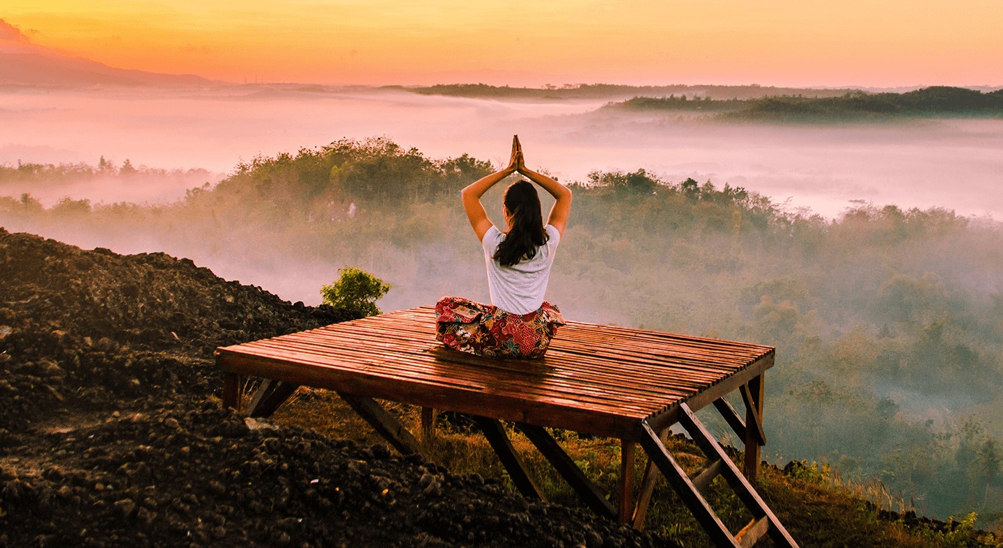 Eine Frau in einer Yoga-Pose bei Dämmerung vor dunstigen Wäldern