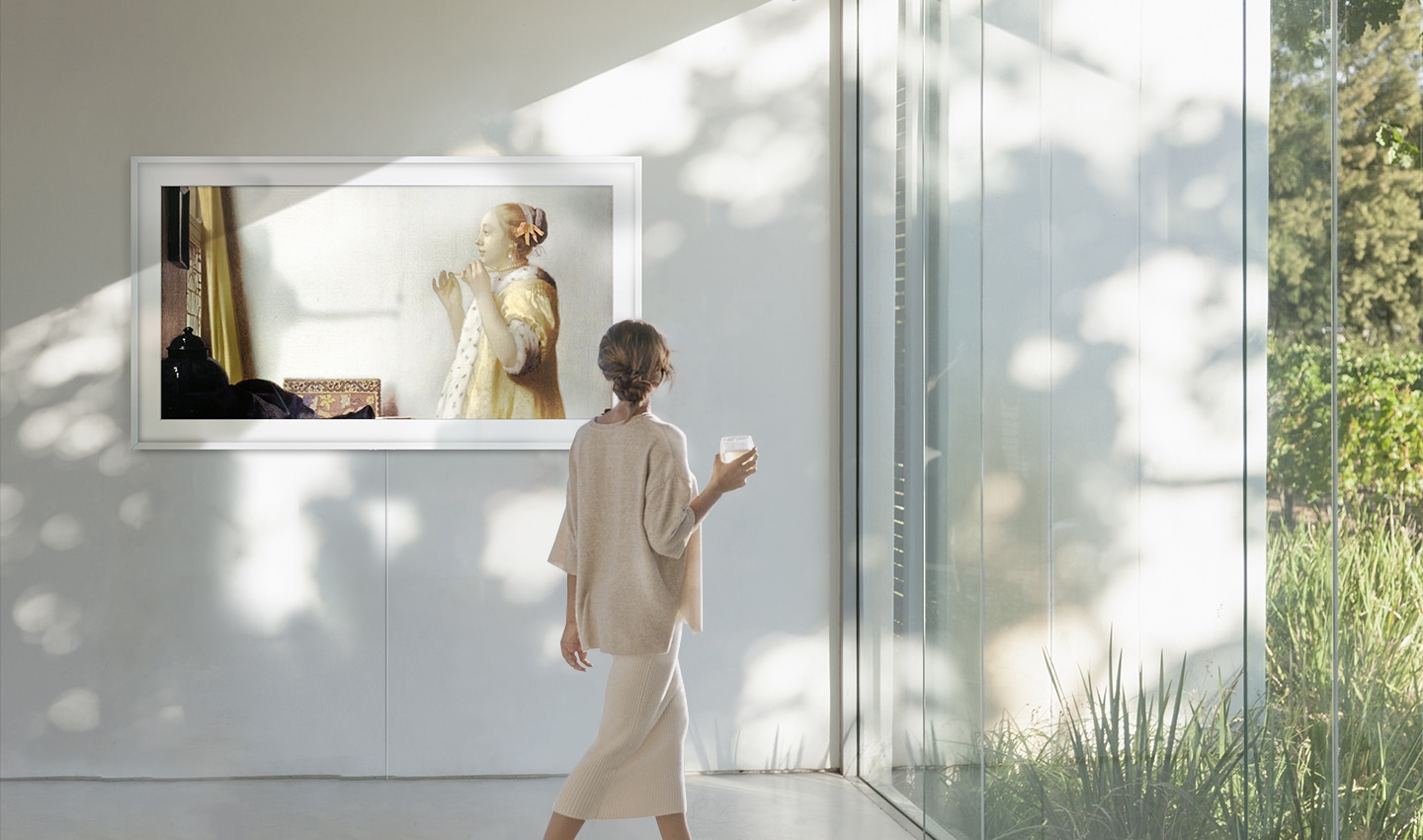 햇살이 환하게 들어오는 공간에 The Frame이 걸려 있습니다. 화면에는 요하네스 베르메르의 <진주 목걸이를 한 여인>이 띄워져 있어 마치 갤러리 같은 분위기가 연출됩니다. 한 여성이 지나가며 작품을 보고 있습니다.