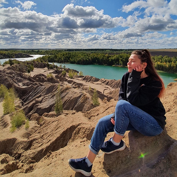 A woman sitting on rock mountain smiling with her eyes closed