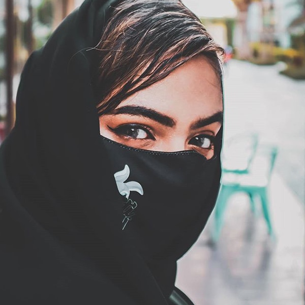 امرأة تبتسم بعينيها وترتدي الحجاب وقناع الوجه.