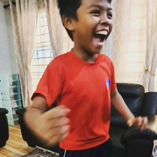 Boy in a red shrit smiling and raising his arms in the air the joy