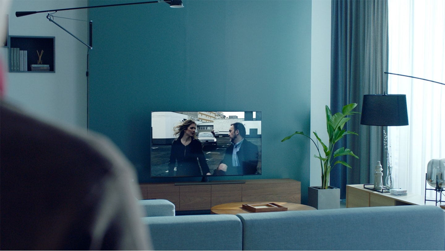 삼성 스마트TV가 거실 벽에 걸려 있습니다. 한 남성이 스마트TV에서 영화 콘텐츠를 보고 있습니다.