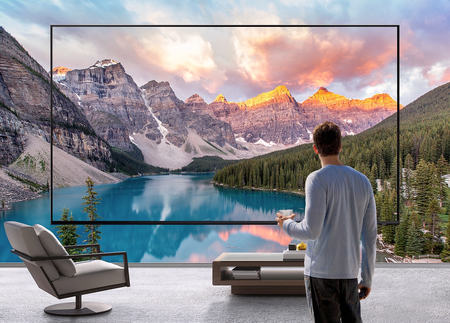 하나의 초대형 TV앞에 커피잔을 들고 있는 남자가 서 있고, TV 화면 너머까지 펼쳐지는 산과 강의 풍경 장면을 보여줍니다.