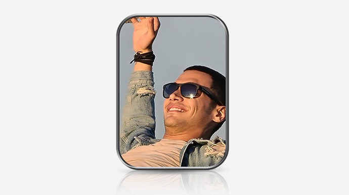 A closeup view of a man in sunglasses, smiling. His right arm is raised and outstretched to the sky.