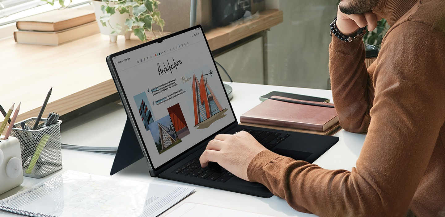 A man is using a Galaxy Tab S9 Ultra with his hand on the keyboard of a Book Cover Keyboard.