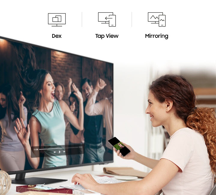 A smiling woman mirrors videos from her phone to her monitor. At the top are the DeX, Tap View, and Mirroring icons.