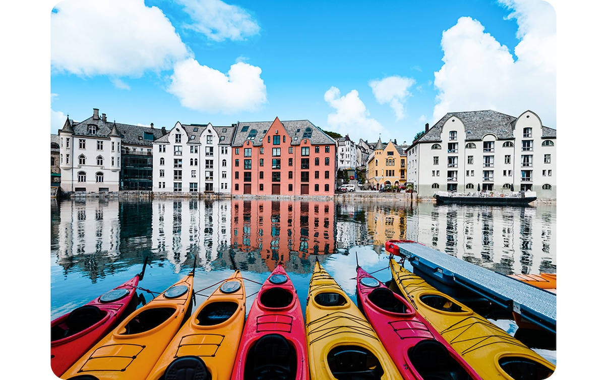 Ultra-wide angle icon activated, the shot includes much more of the canoes, more buildings in the background and more of the sky. Ultra-wide angle are above a landscape of yellow and red canoes lined up in a pier with white and red buildings in the far background. "