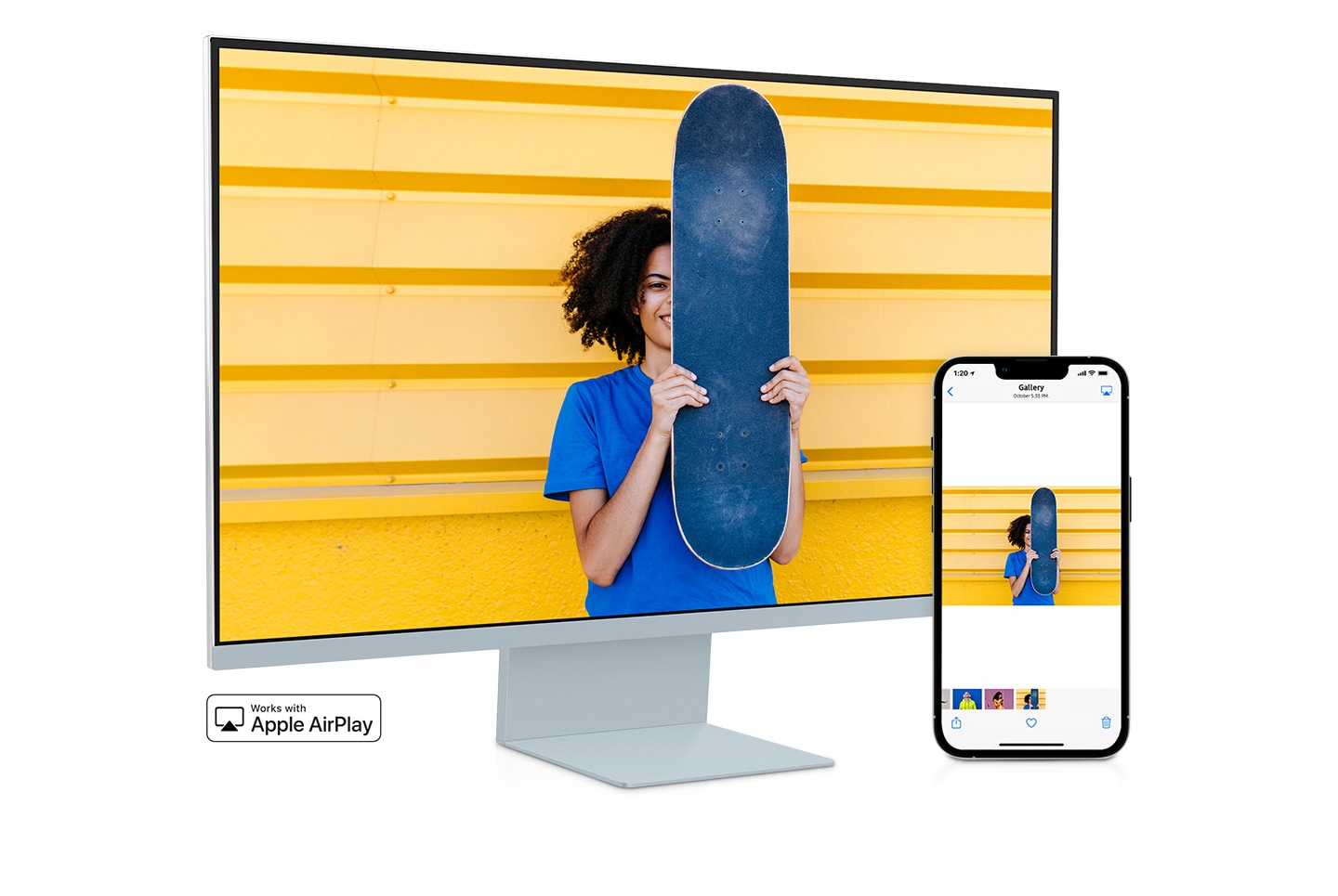 A smartphone and monitor sit side-by-side. The smartphone shows a woman posing with a skateboard. The same woman with skateboard is shown on the monitor. The smartphone's gallery app swipes through different photos which are also shown on the monitor screen.