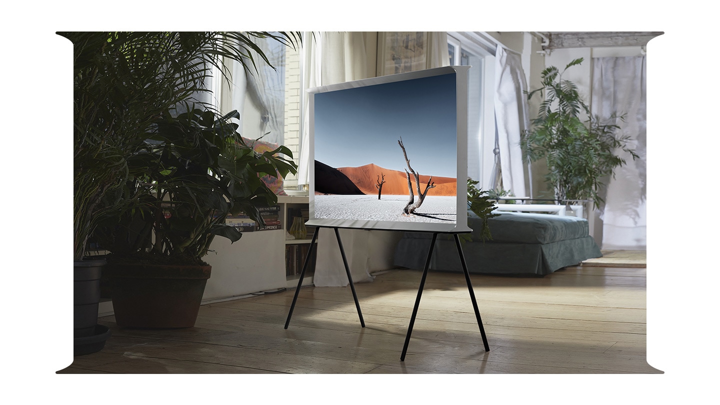 The Serif is mounted on a floor stand in a living room with many plants.