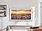 The Frame is hanging on a wall in a living room displaying a sunset over a city.