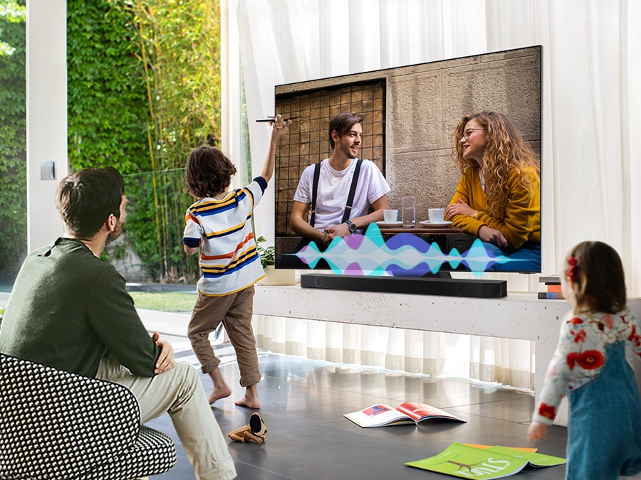 A man watches TV while his children play. Simulated sound wave graphics show Active Voice Amplifier technology optimizing dialogue so it can be heard more clearly in noisy environments.