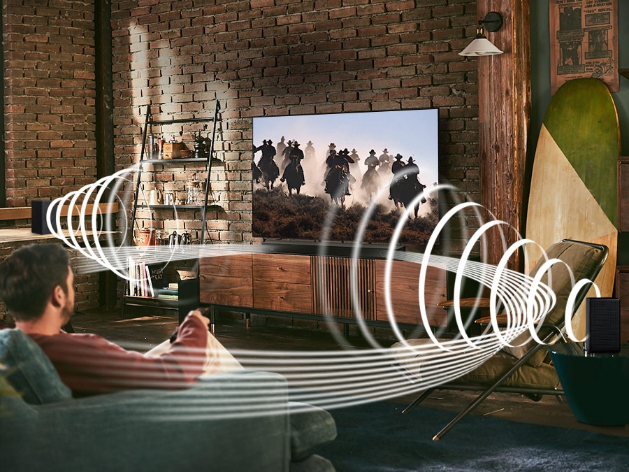 A man enjoys racing content on his TV. Samsung Wireless Rear Speaker Kit and Soundbar create Immersive surround sound. Toggle button is shown.