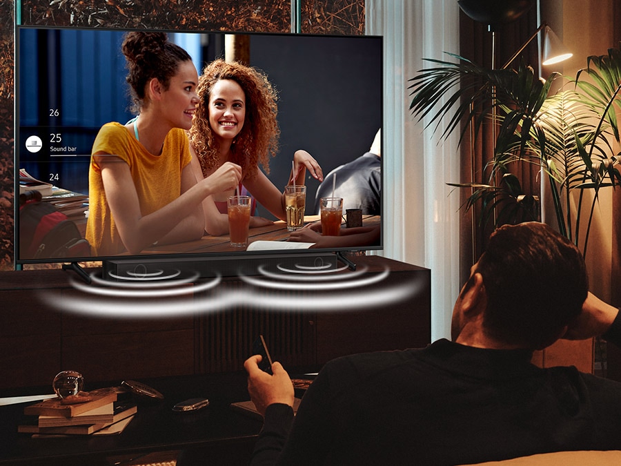 A man is watching his Crystal UHD TV at night with the Soundbar optimally adjusted in Night Mode. The sound from the soundbar's side speakers are emphasized during the night.