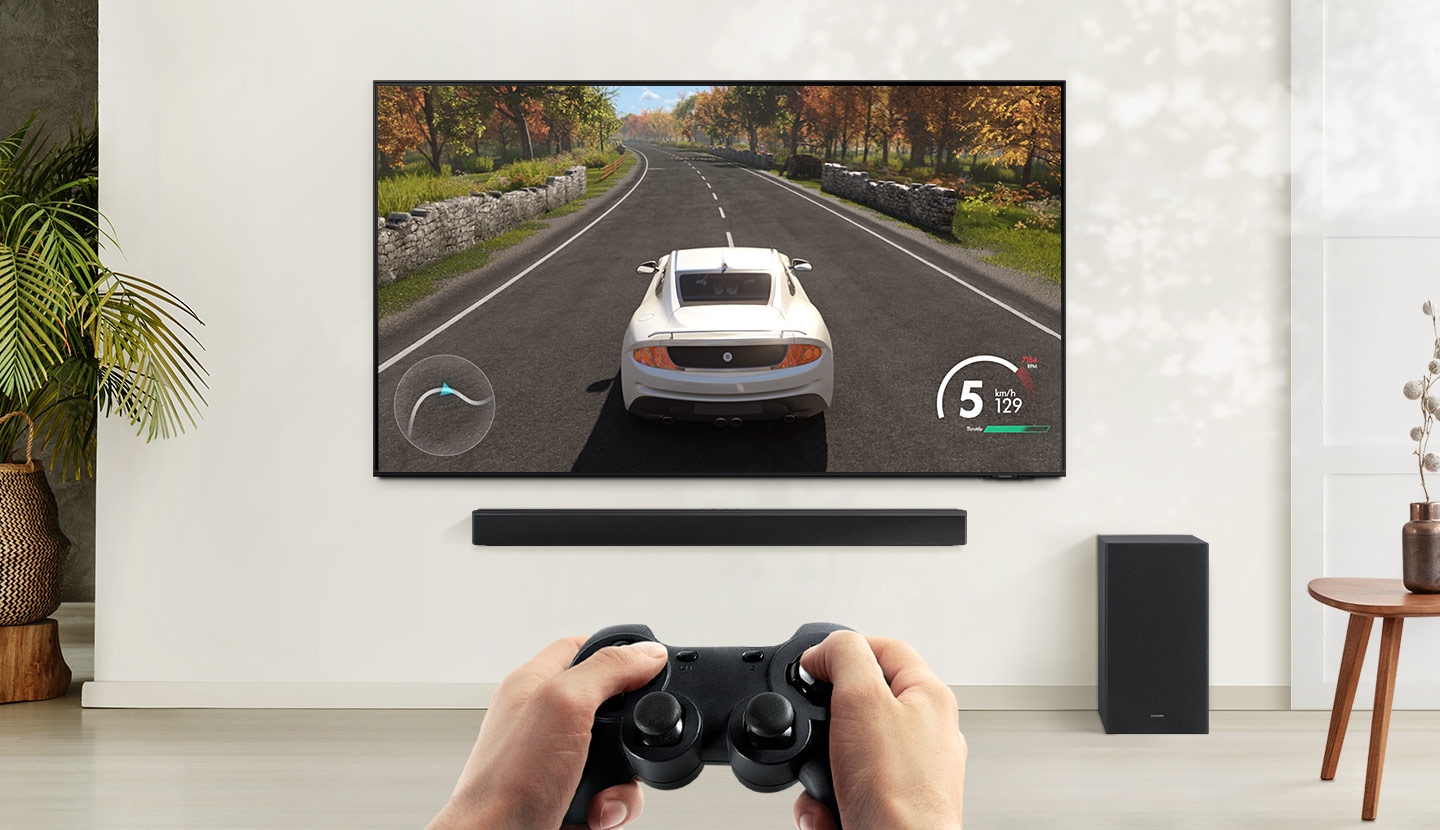 A user is enjoying soundbar’s Game Mode while playing a racing game on their TV connected to soundbar and subwoofer.