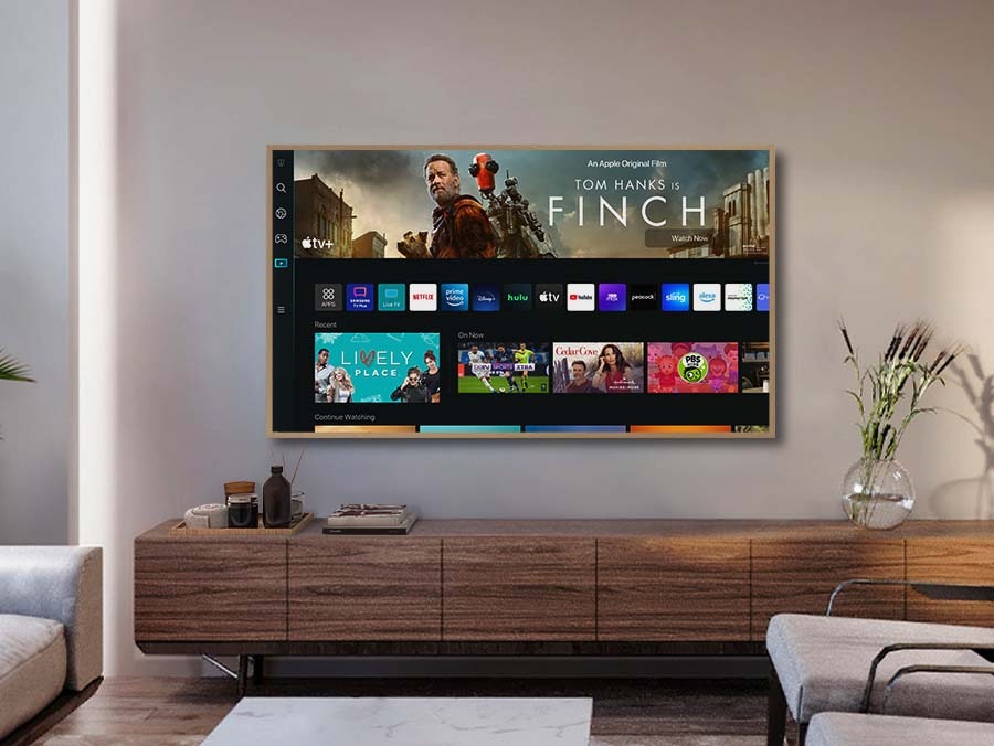 A girl is pointing the remote towards The Frame, which shows the Smart Hub home screen.