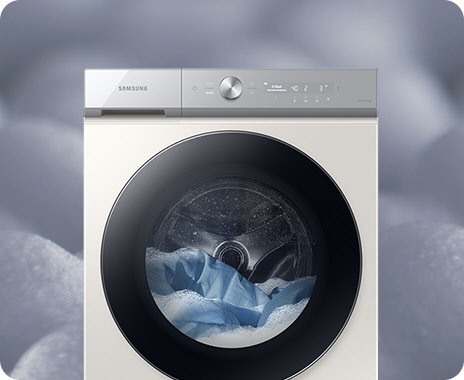 A front facing white Samsung Bespoke Grande AI washer is set with detergent foam. The washer is in mid-cycle, with laundry and detergent bubbles inside the machine.