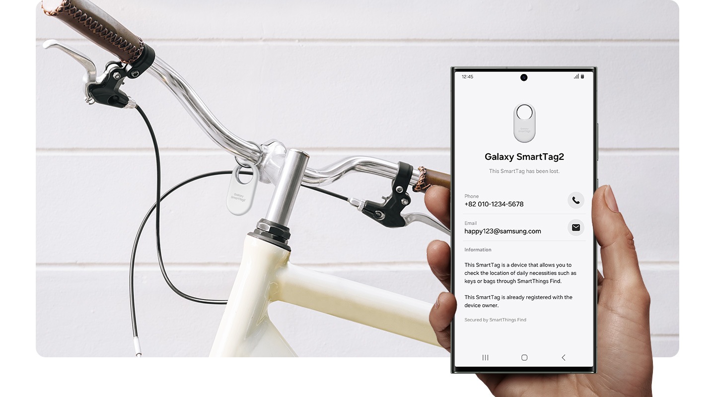 in the background, a bicycle handle is shown with a galaxy smarttag2 device tagged. in the foreground, a hand holding a galaxy smartphone device shows the galaxy smarttag2 device's registered information on lost mode.