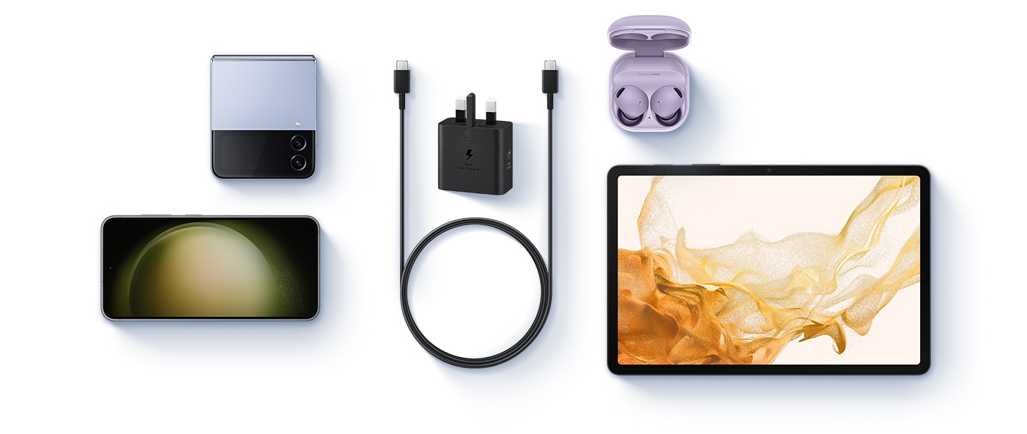 A birds-eye-view of various devices are shown with a black Power Adapter and a USB-C cable placed at the center. To the left, a Blue Galaxy Z Flip4 and a Galaxy S23 are shown. To the right, Buds 2 Pro in Bora Purple and a Galaxy Tab S8 are shown.