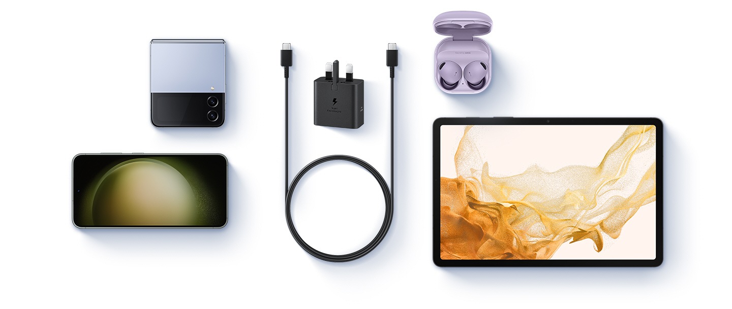 A birds-eye-view of various devices are shown with a black Power Adapter and a USB-C cable placed at the center. To the left, a Blue Galaxy Z Flip4 and a Galaxy S23 are shown. To the right, Buds 2 Pro in Bora Purple and a Galaxy Tab S8 are shown.