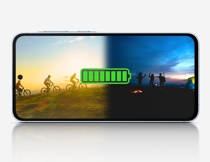 A Galaxy A55 5G showing a battery icon at full charge overlaying an image of people enjoying outdoor activities. on the left, cyclists are riding at sunset, and on the right, a group is gathered around a campfire in the evening.