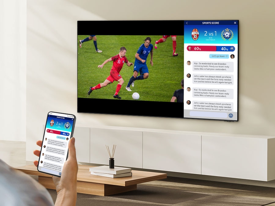 A person watches 2 different screens on their TV simultaneously. They have one screen displaying a soccer match and the second screen mirroring their mobile with live stats.