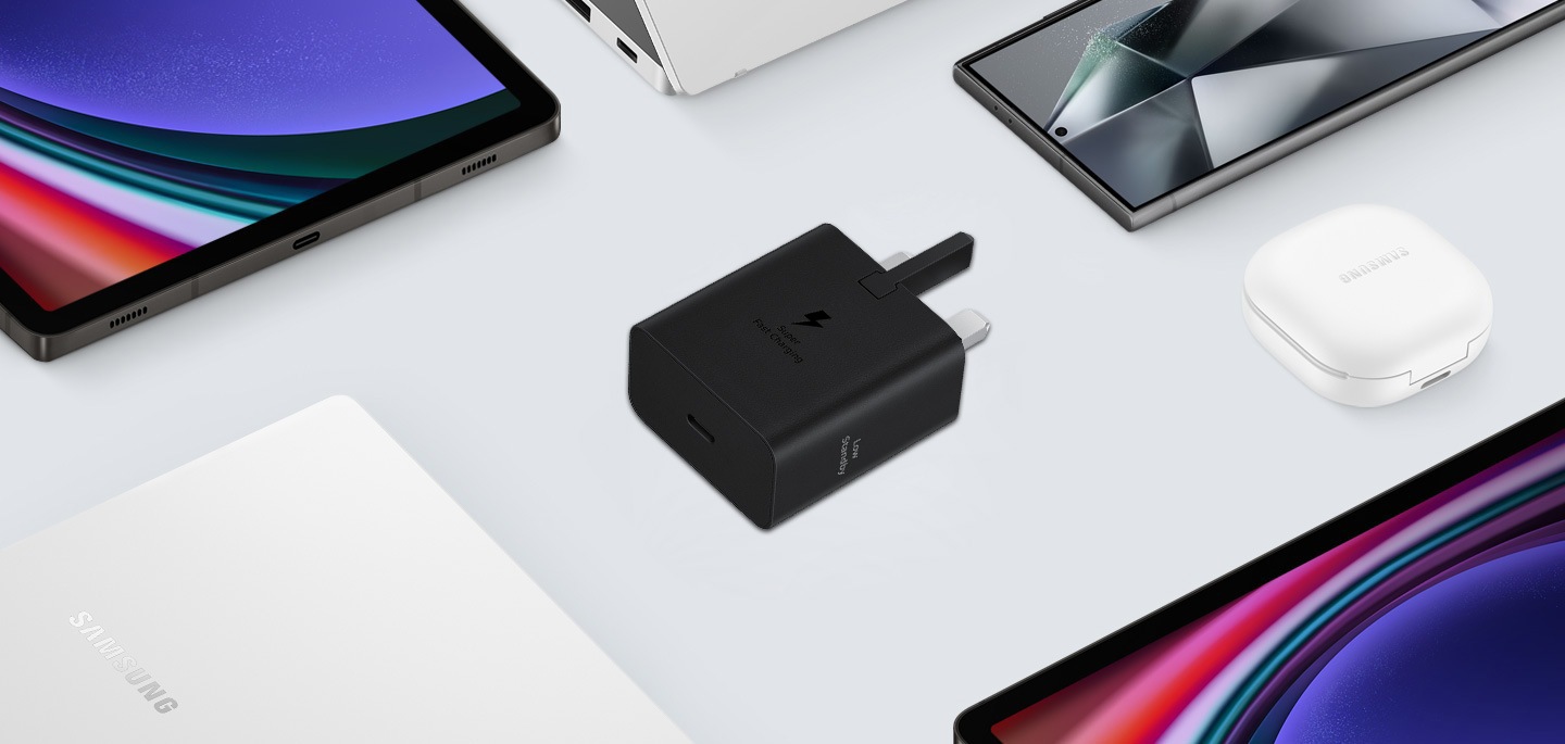 A top view of various Samsung Galaxy devices are shown with a black Power Adapter placed at the center. To the left, a Galaxy Book3, to the right Galaxy Buds2 Pro in White, a Galaxy Tab S9 and Galaxy S24 Ultra are also shown.