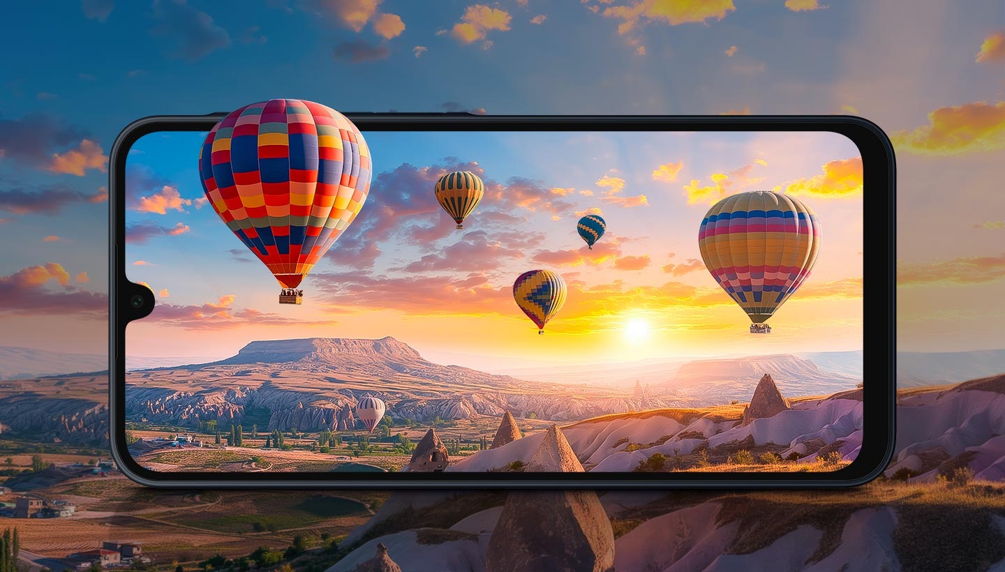 In the background, a canyon landscape at sunset with colorful hot-air balloons floating in the sky. In the foreground, a Galaxy A16 5G device displays its FHD+ Super AMOLED screen, bringing the landscape to life with clearer details and more vivid colors. One balloon appears to float out of the screen, highlighting the immersive viewing experience.