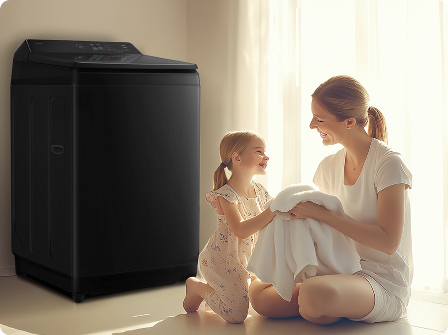 A mother and daughter are sitting in front of a washing machine, touching towels. 