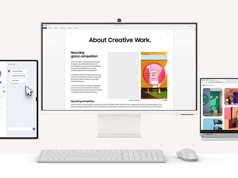 There is a monitor in the middle, with a laptop and a tablet around it. All devices are controlled by a mouse. The cursor selects an image from the laptop and drags and drops it into a file opened on the monitor.