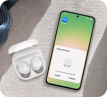 White Galaxy Buds Core in their charging case next to a Samsung Galaxy smartphone with the pairing pop-up on screen.