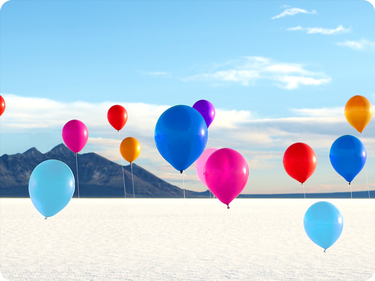 Colorful balloons float in the air against a snow-covered field and beautiful blue sky in the background.