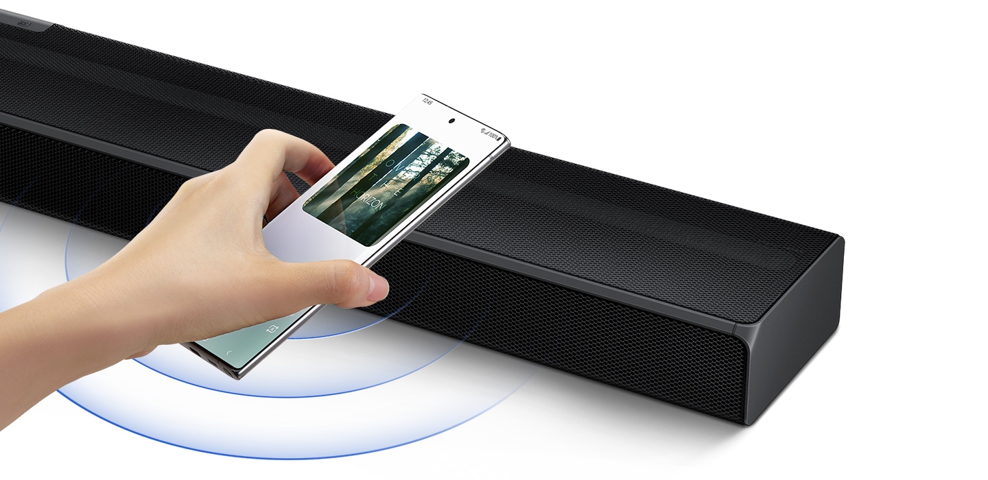 A hand taps a smartphone with the Samsung music app on-screen on the soundbar and the soundbar instantly plays music, showing how easy it is to switch from smartphone to soundbar.