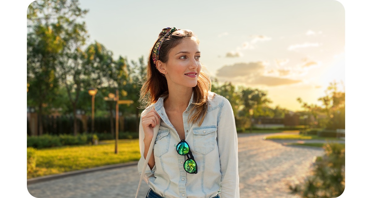 High quality portrait shot of a woman looking to the side, with grass patched road under clouds and sunlight in the background blurred out.