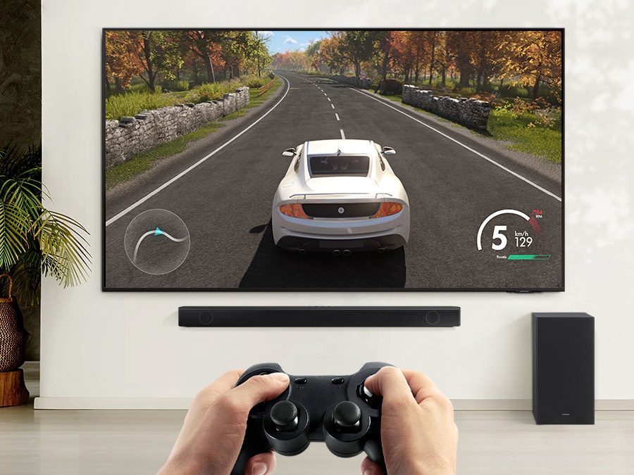 A user is enjoying soundbar’s Game Mode while playing a racing game on their TV connected to soundbar and subwoofer.