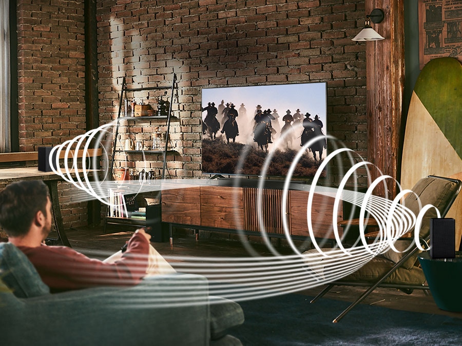 A man enjoys racing content on his TV. Samsung Wireless Rear Speaker Kit and Soundbar create Immersive surround sound. Toggle button is shown.