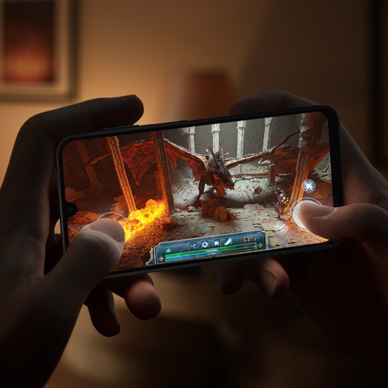Two hands gripping a Galaxy A16 device, engaged in a graphic-heavy video game in a dimly lit room.