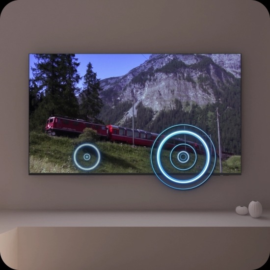 A TV depicts a scene of a train passing by a scenic outdoor location. As it does, sound waves appear near where the train touches the tracks, indicating the noise within the scene.