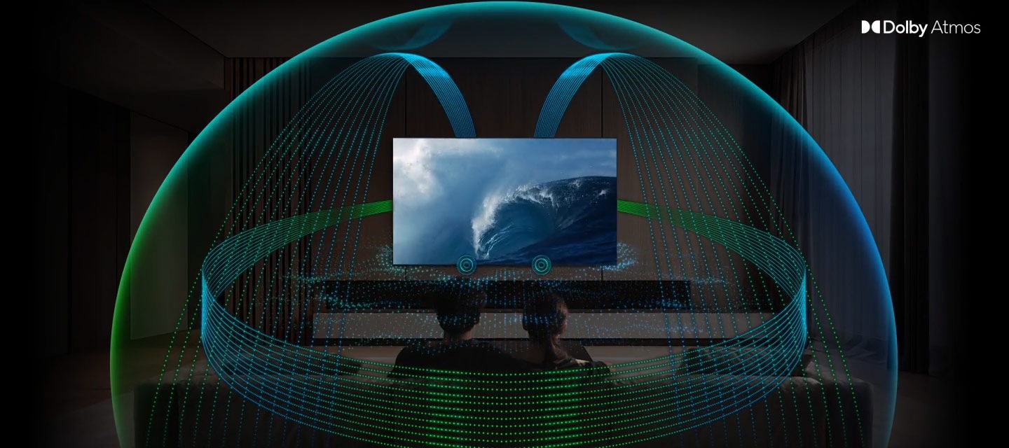 In a living room, a couple sits on a sofa and watches TV. The TV’s front speakers are lit up and soundwaves emanate from a TV’s side and up-firing speakers, travelling in multiple directions to surround the couple in a dome of sound and fill the room. Dolby Atmos logo.