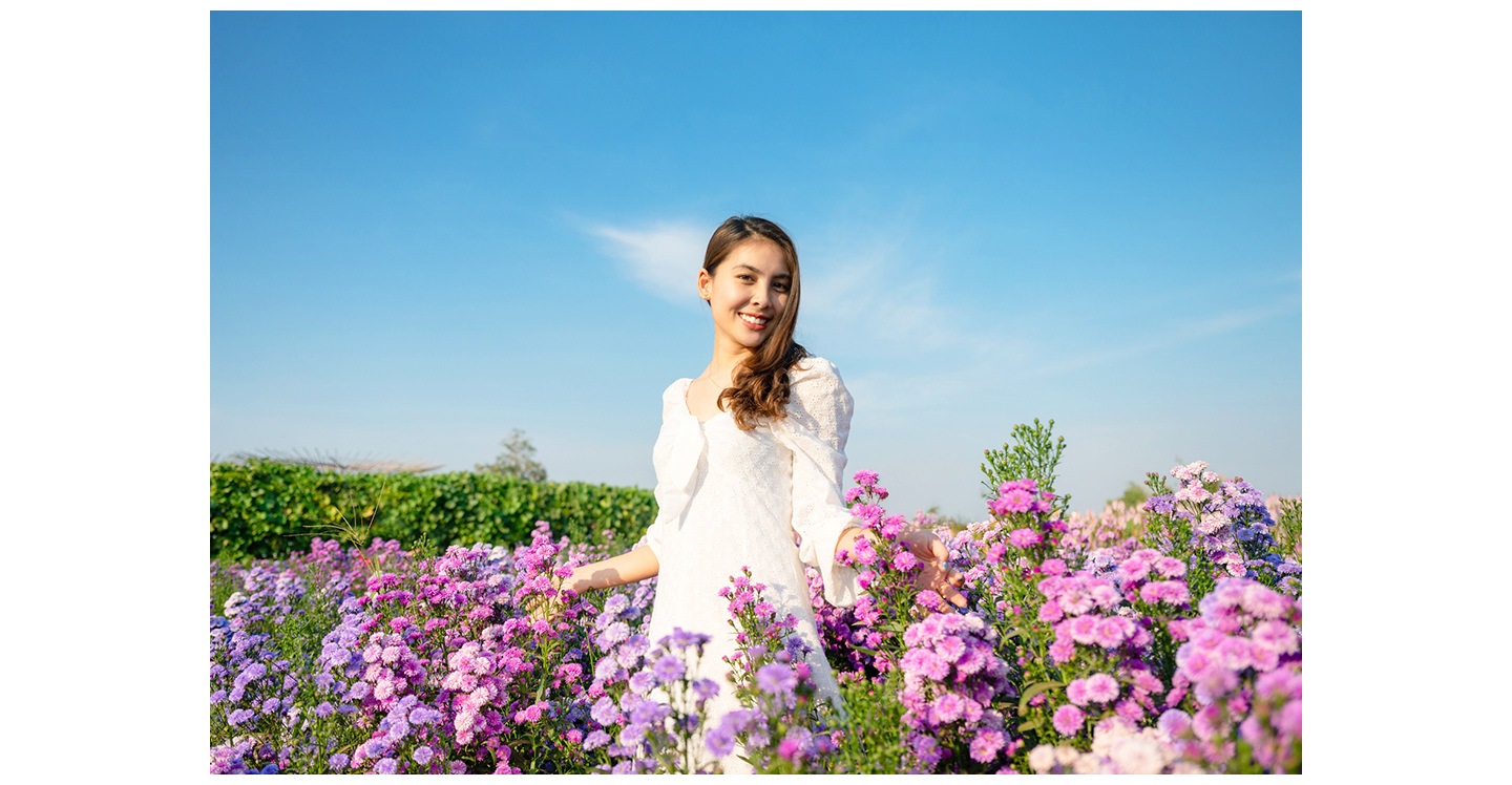 A woman in a white dress standing outdoors among many flowers, posing for a photo.
