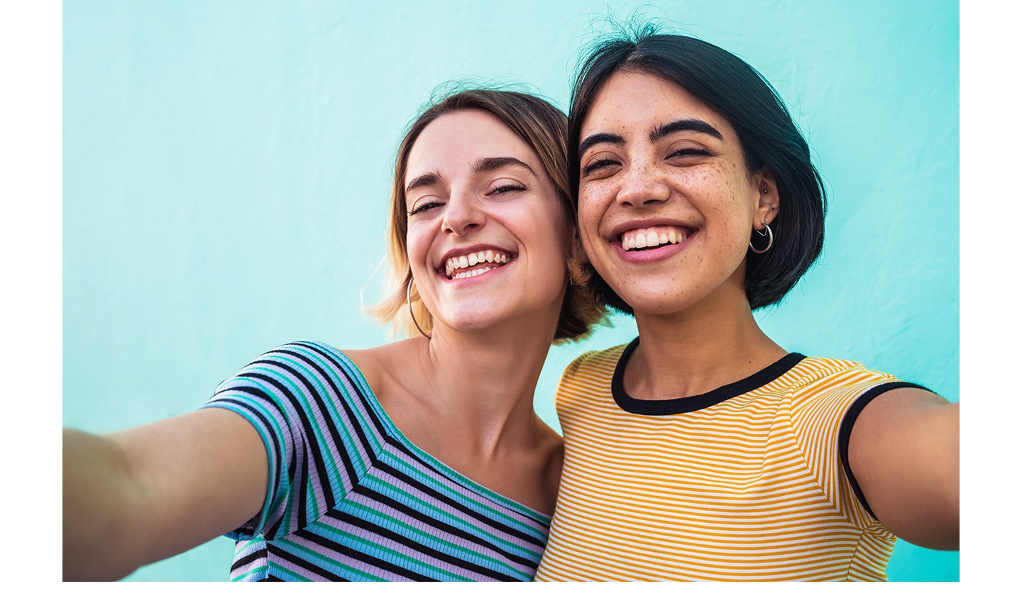 Two women smiling while taking a selfie together using Galaxy A27 5G's 12 MP Front Camera. The selfie looks clear and natural with lively colors, sharp details and optimal exposure.