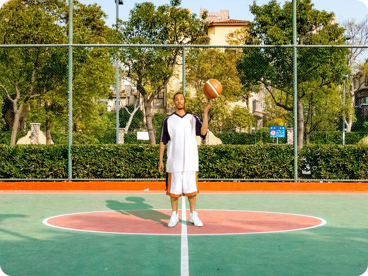 1. A man standing in a basketball court. It is a close crop shot, showing the man and the center of the court.