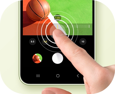 Una mano toca la pantalla de un Galaxy A34 5G, cambiando la relación de zoom de una foto de una pelota de baloncesto.