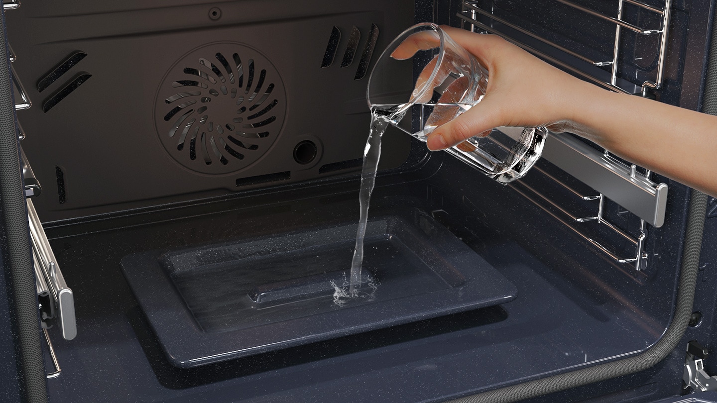 Shows a person pouring water from a glass into a dedicated tray on the bottom of the oven, which is used to create steam.