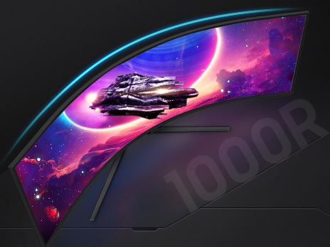 The curved monitor shows a spaceship flying in front of a planet, and toward futuristic buildings. Below the monitor, text reads 