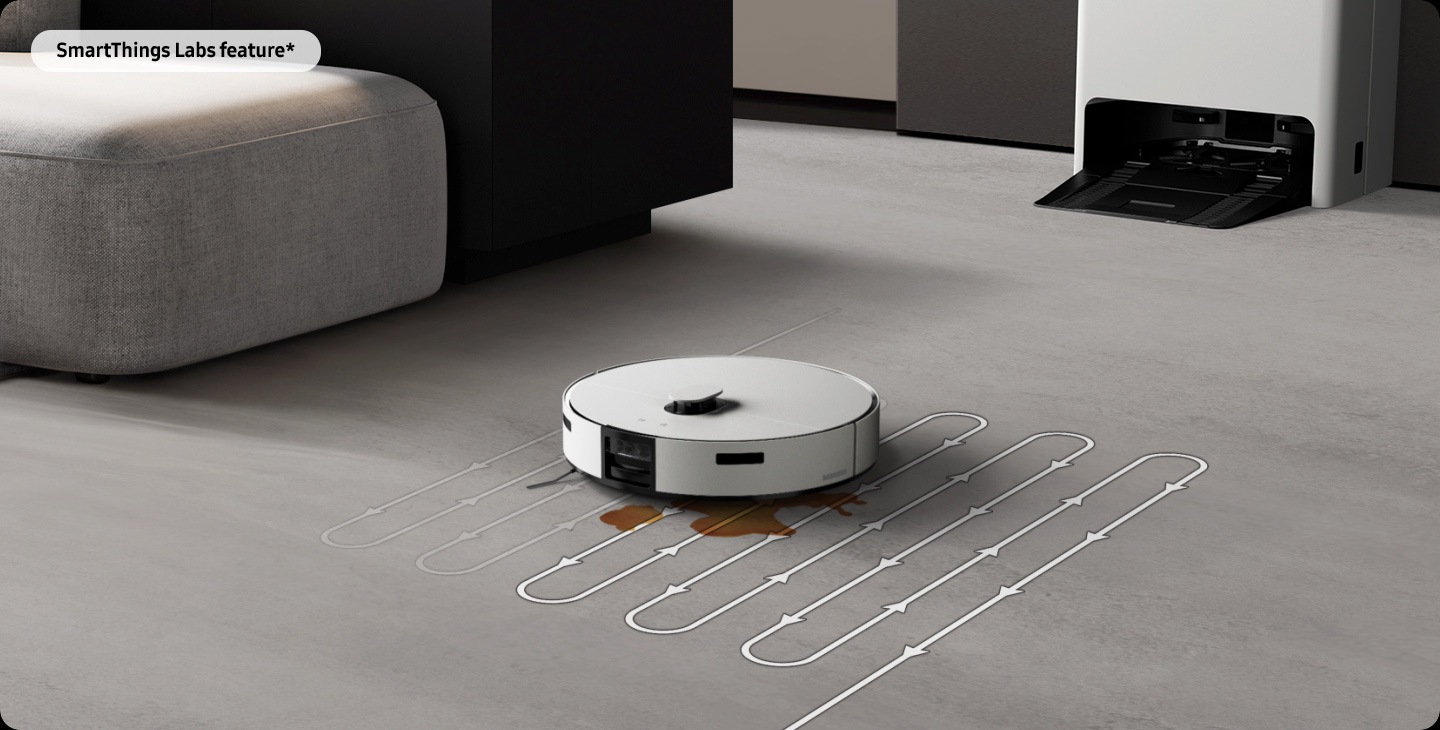 Jet Bot Combo AI Steam+ detects a stain on the floor. It moves to the Clean Station Steam+ to prepare heated wet mop pads, then returns to the stained area to deep clean it with a zigzag course. SmartThings Labs Feature* text is in the top left corner.