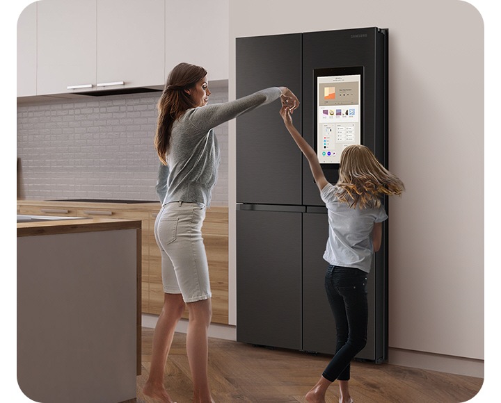 A mother dances with her child in a stylish kitchen in front of a Family Hub. The display has a music app and a playlist.