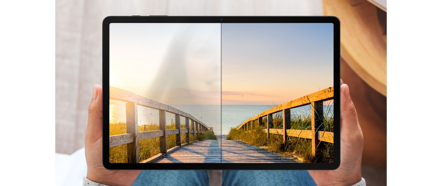 A woman holds a Galaxy Tab S8+ in her hands. The wallpaper onscreen has a bridge and the ocean. Half of the screen is covered with the screen protector film and the other half isn't. The side with no film has a reflection of the woman's face whereas the side with the film has no reflection and the colors are more crisp and clear.