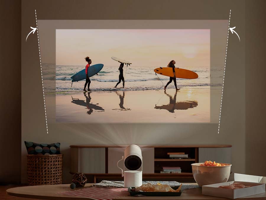 The Freestyle is projecting an image of three people carrying surfboards at a beach onto a slanted wall. The image is slanted due to the wall, but The Freestyle automatically adjusts it to make it level.