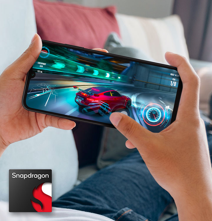 Two hands holding a Galaxy A05s shows racing gameplay on-screen. At the bottom left corner, the Snapdragon logo is shown.