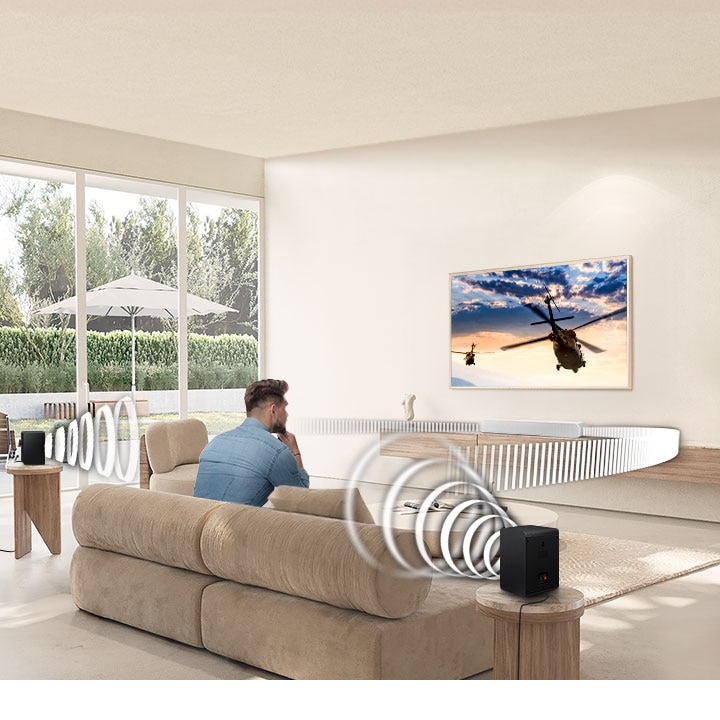 A man watches TV. A Soundbar and rear speakers give off sound waves of various types, traveling in different directions.